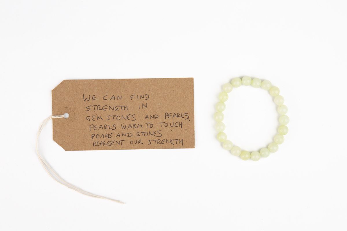 A pearlescent coloured pearl bracelet. With a brown, handwritten luggage tag