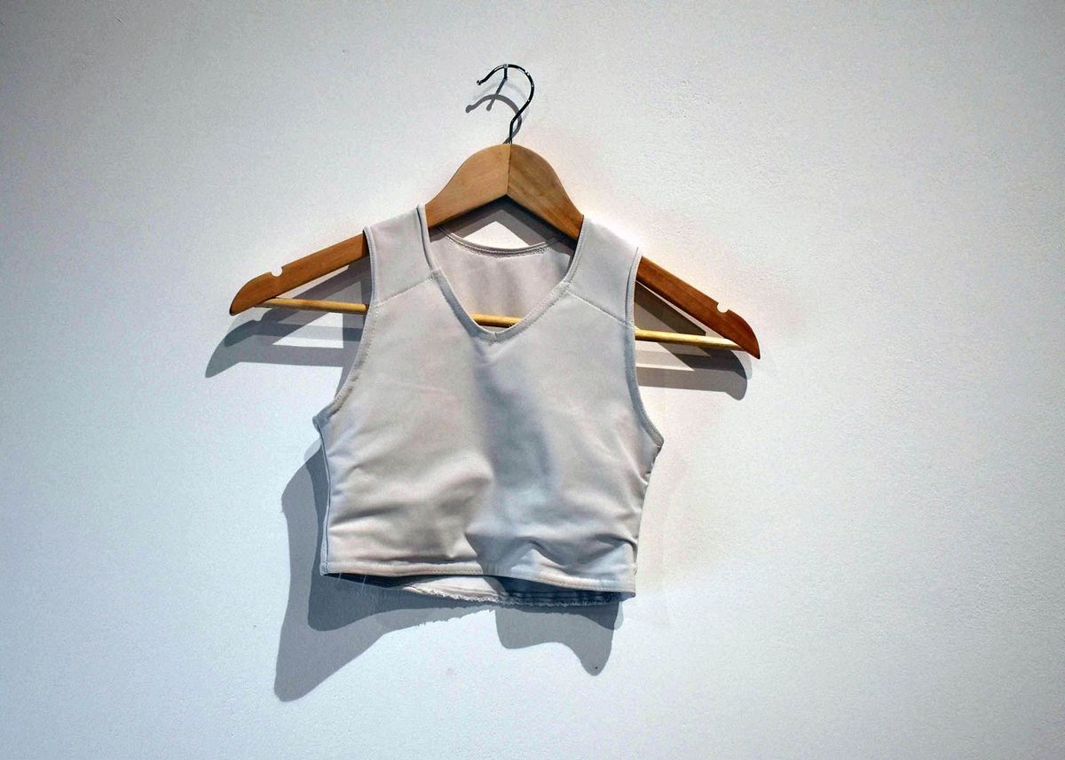 A light gray crop top on a wooden hanger is displayed against a plain wall.