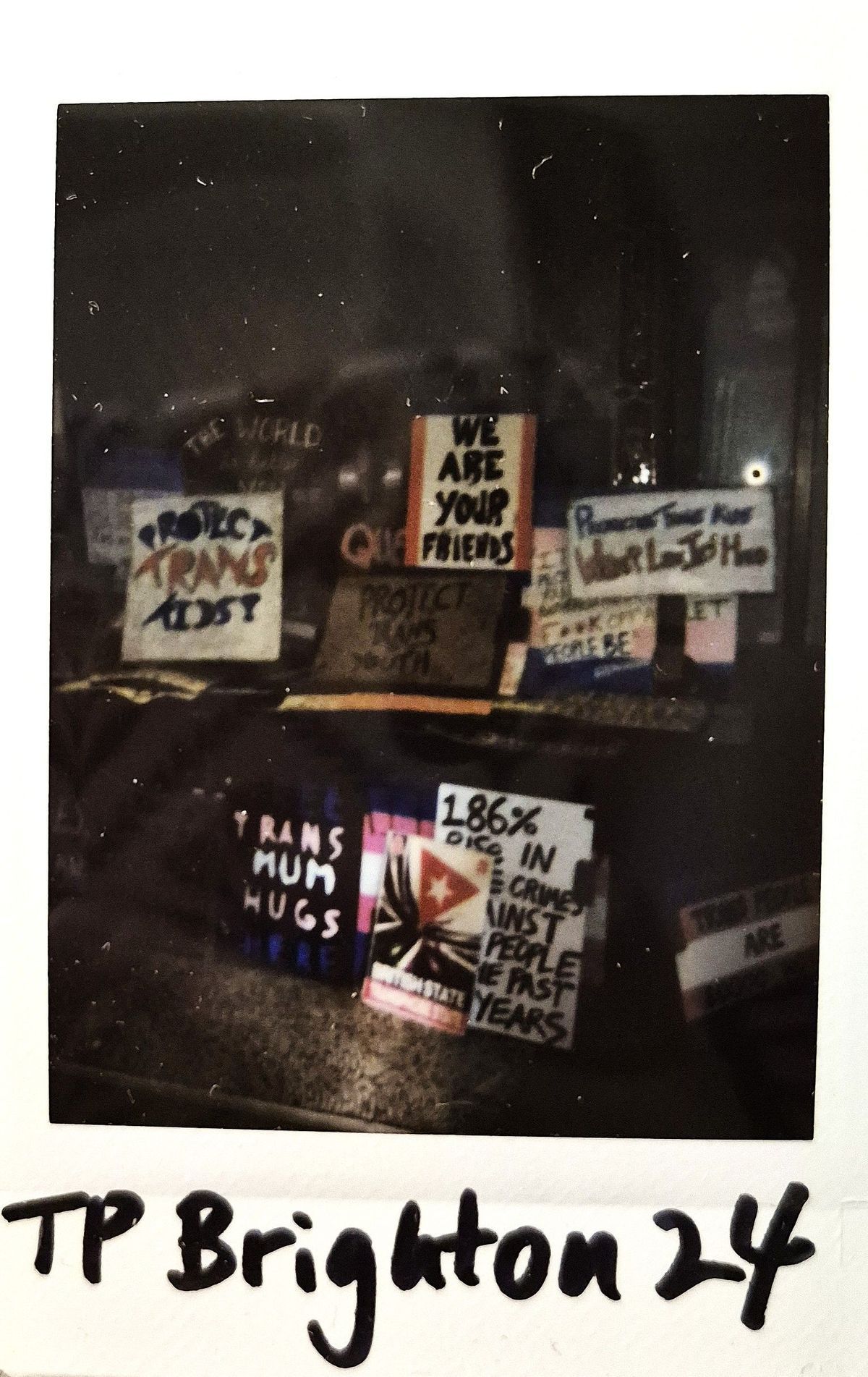 Lots of protest signs propped up together against a fence at night time.