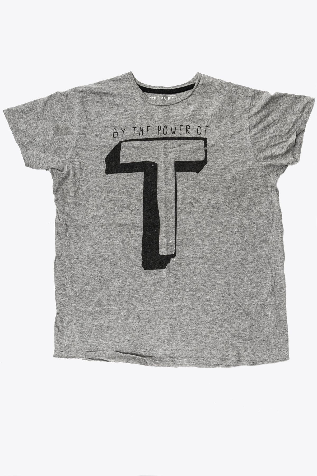 A grey t-shirt with the text "BY THE POWER OF" above a large black "T".