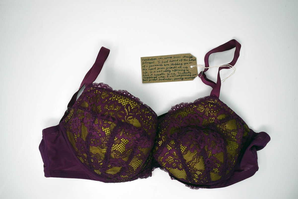 A burgundy lace bra lies on a white background, accompanied by a small handwritten note.