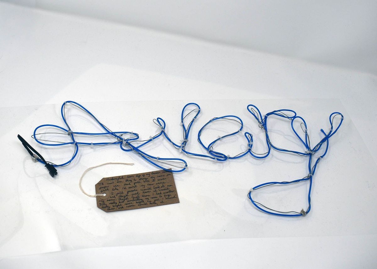 Blue wire spelling "Rock" lies on a surface, accompanied by a handwritten tag.