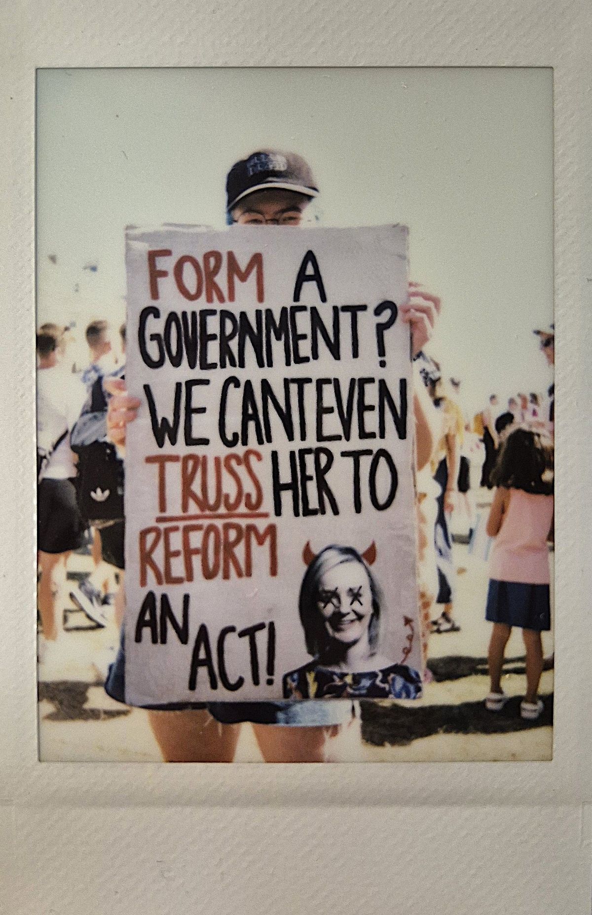 A person holds a protest sign with bold text which says "FORM A GOVERNMENT? WE CAN'T EVEN TRUSS HER TO REFORM AN ACT!".