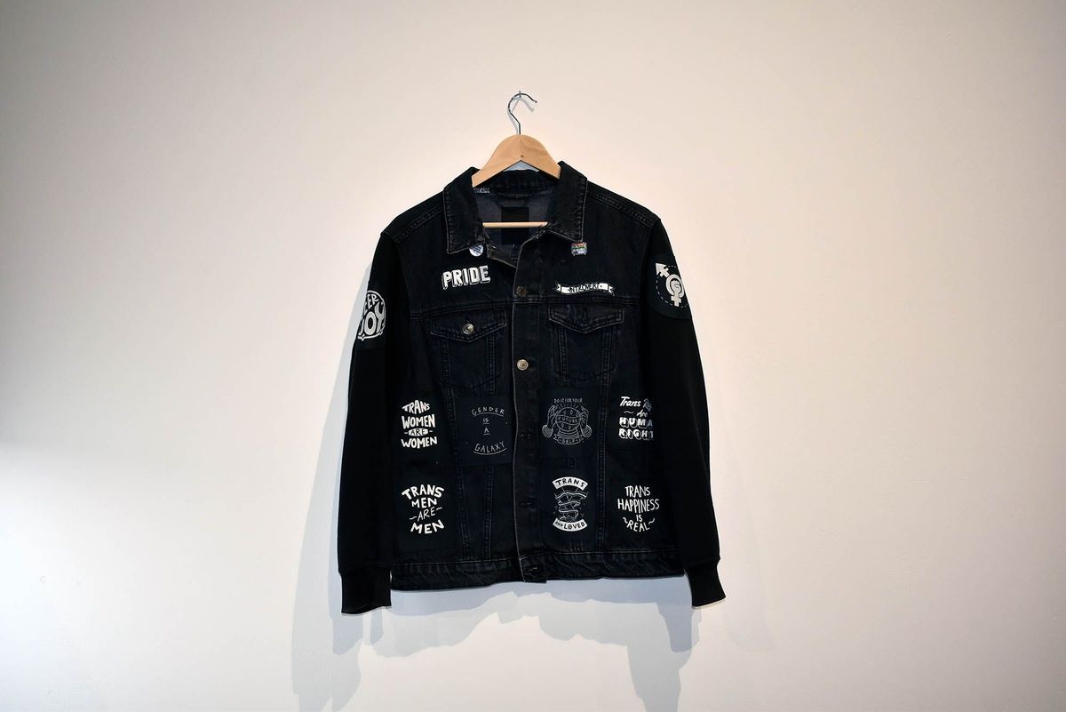 Black denim jacket with cotton padded arms covered with seventeen patches sewn on and three affixed pin badges.