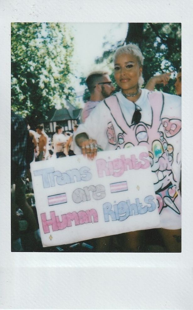 A person is holding a colorful sign that states "Trans Rights are Human Rights" at an outdoor event