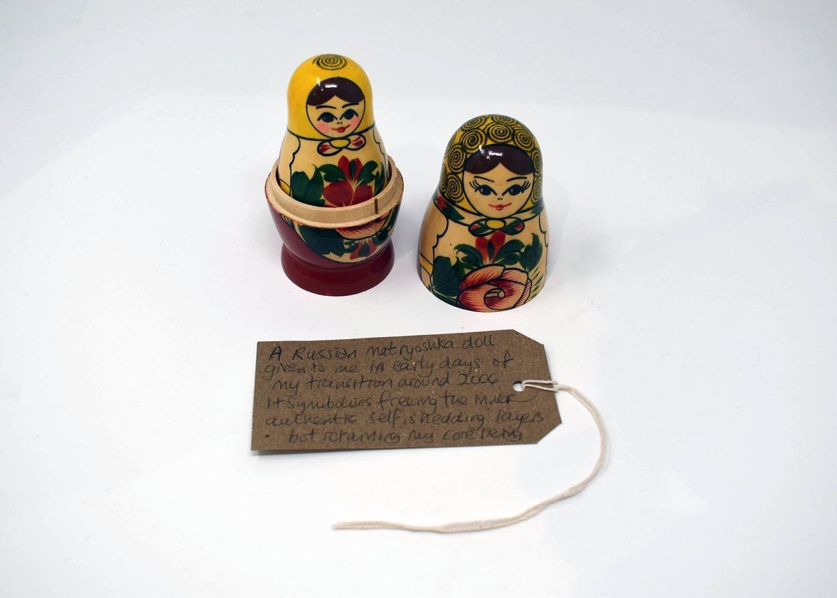 A russian doll which has the first head taken off so you can see the inside doll. It is colourfully painted in reds, yellows and greens.