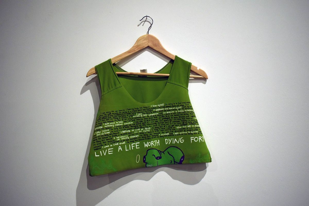 A green binder with handwritten text and illustration hangs on a wooden hanger.