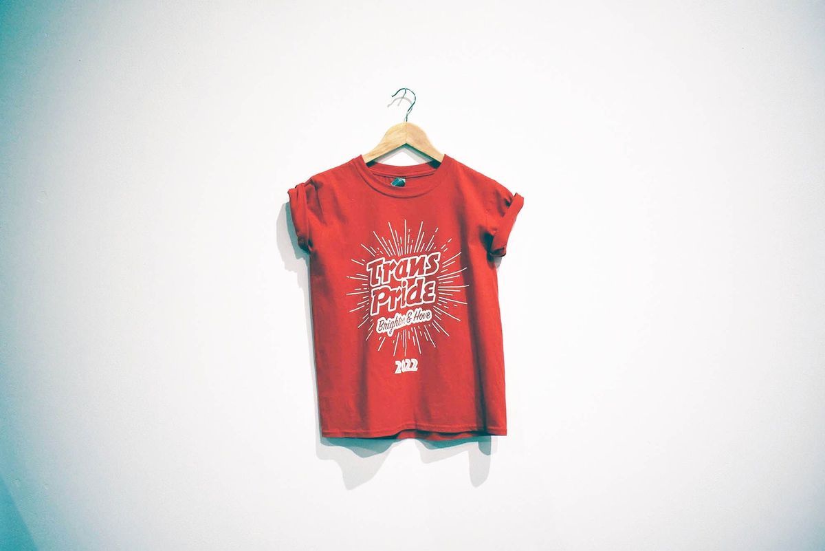 Red T-shirt with a starbust design and the words "Trans Pride Brighton & Hove 2022" printed in white in the center.
