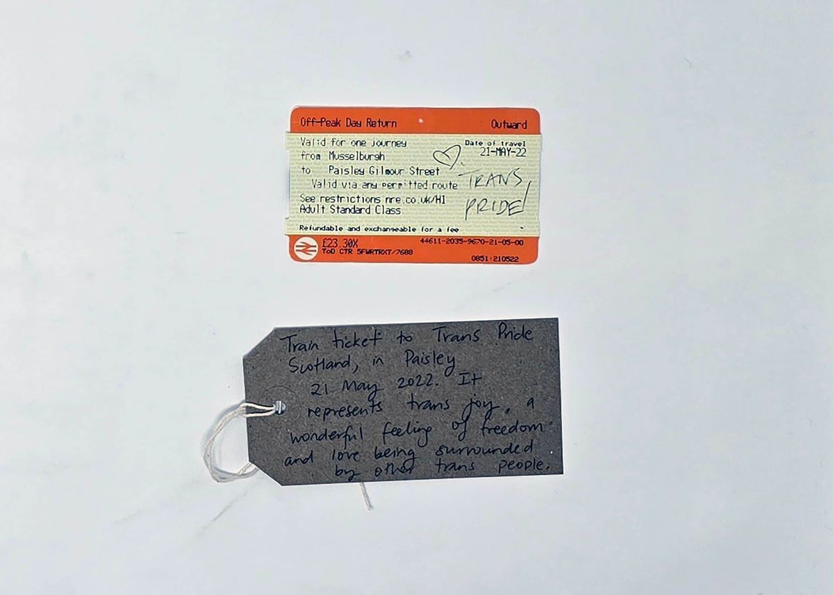 A train ticket which has 'Trans Pride' written in biro on it with a hear. Underneath there is a brown tag with writing on it.