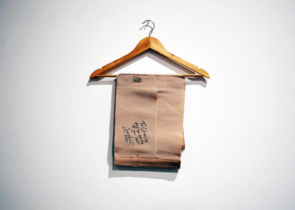 A wooden hanger displays folded beige fabric with handwritten notes on a plain white wall.