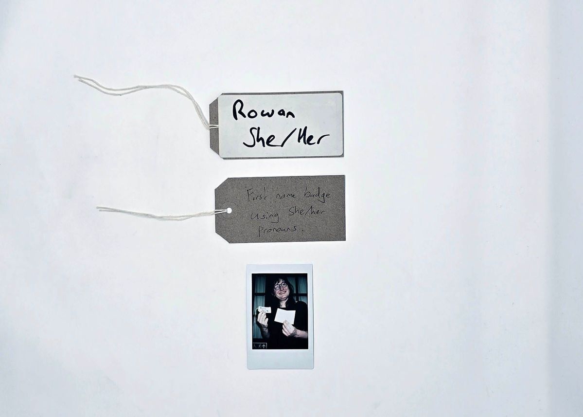 A handwritten name tag inscribed "Rowan" "She/Her". With a brown handwritten luggage tag.