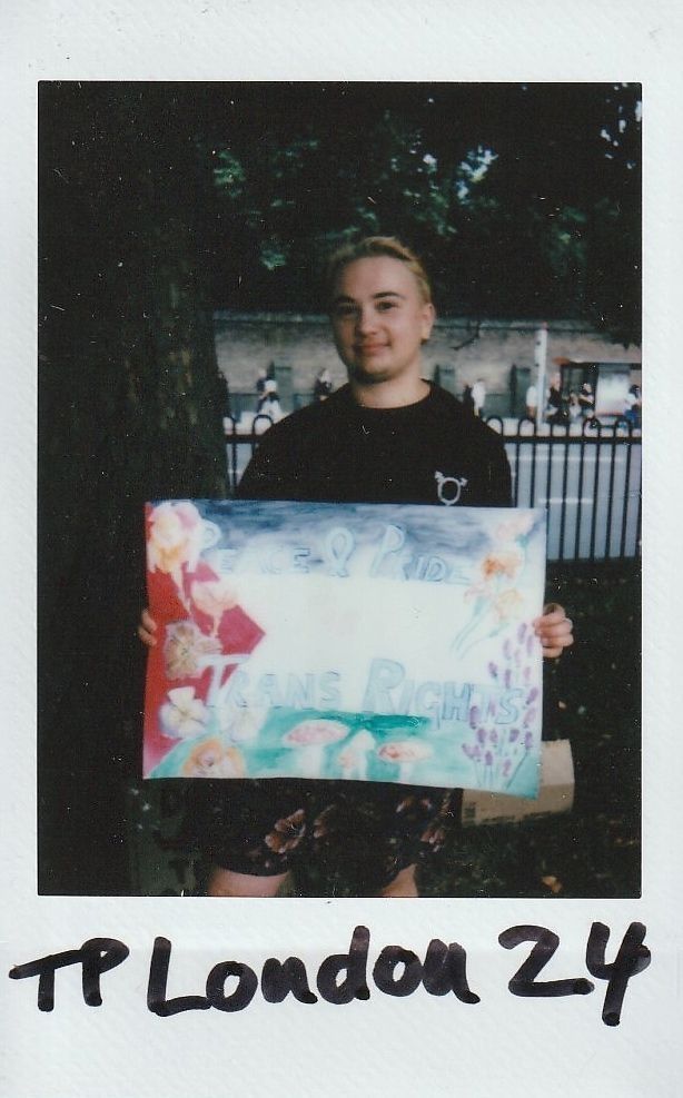 A person holds a colorful sign that reads, “Peace and Pride, Trans Rights".