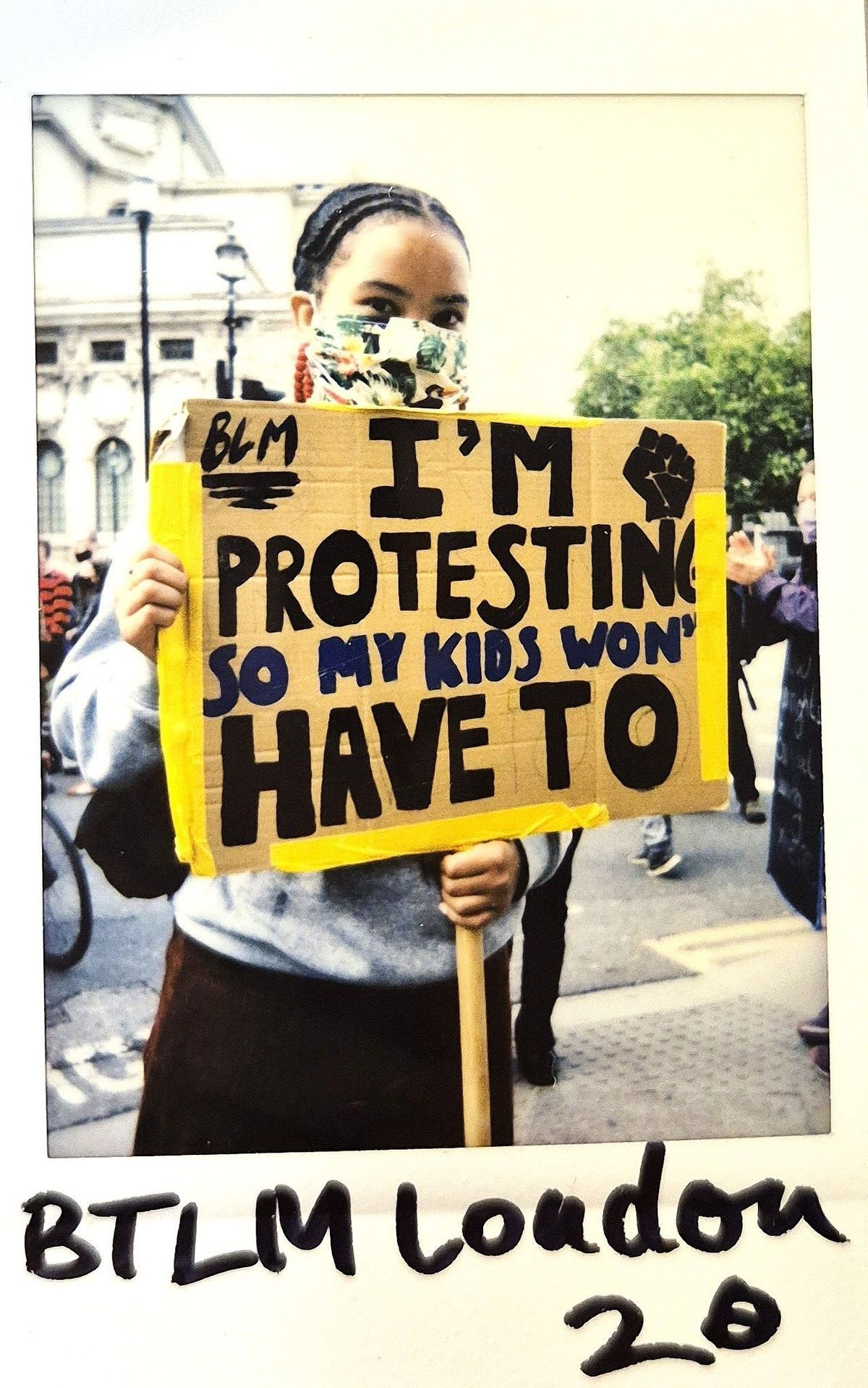 A protester wearing a mask holds a sign that says, "I'm protesting so my kids won't have to".