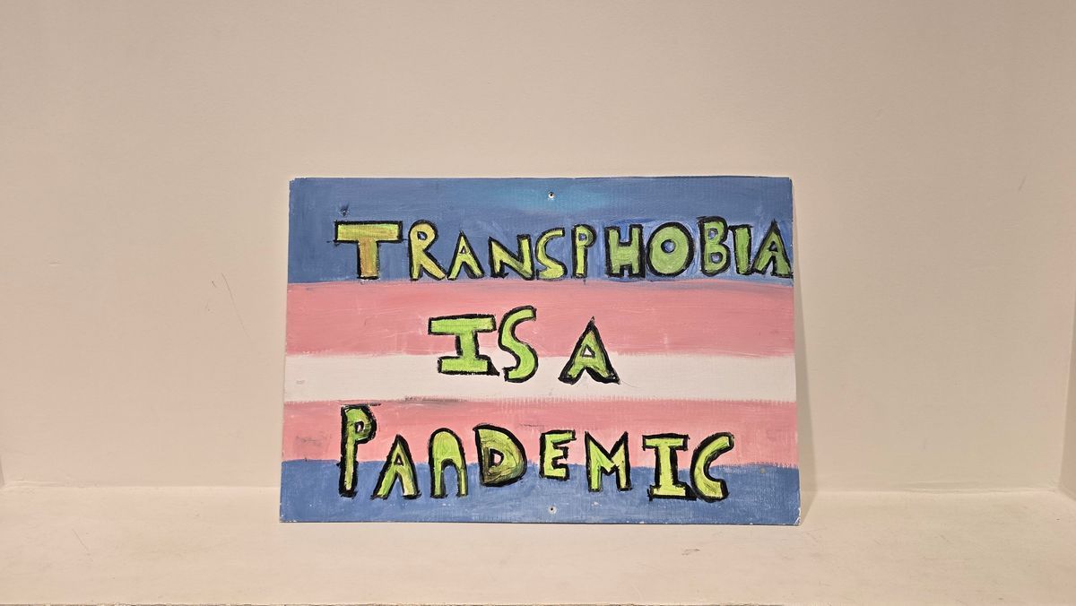 A canvas painted with colors features the message, "Transphobia is a Pandemic," in bold letters