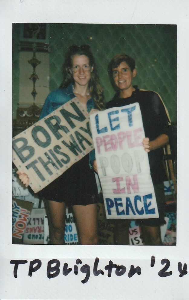 Two people are smiling and holding signs with messages at an event in Brighton.