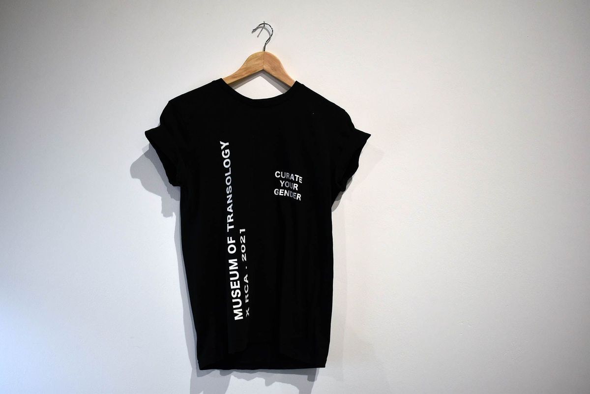 A black T-shirt on a hanger features the text "CURATE YOUR GENDER" and "Museum of Transology".