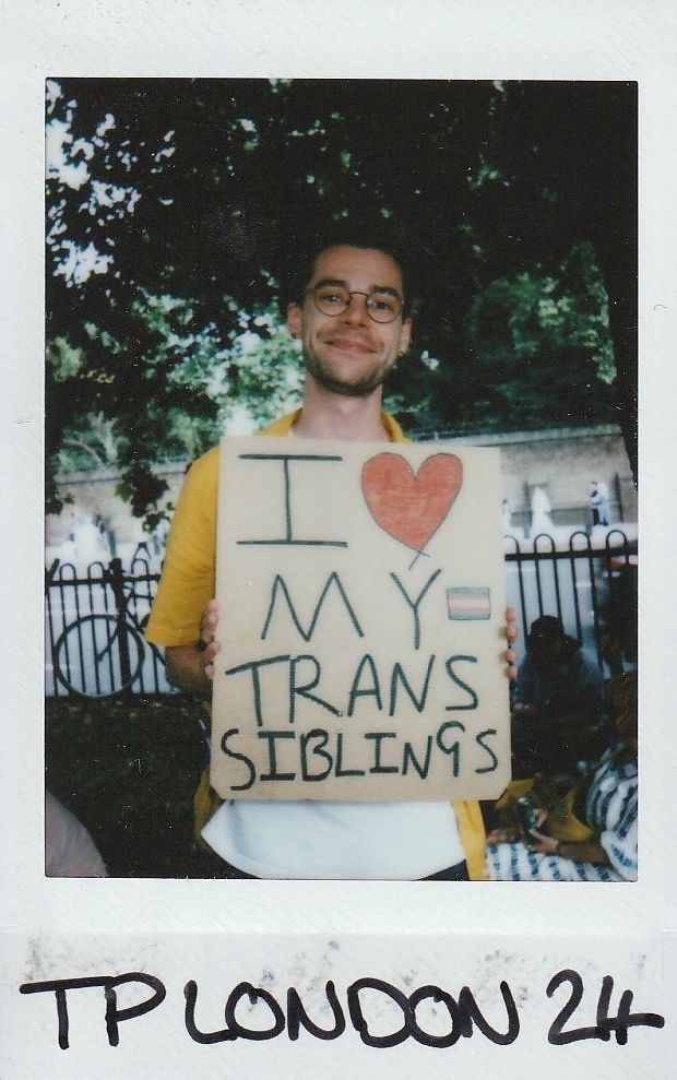 A person is smiling while holding a sign that says, "I love my trans siblings".