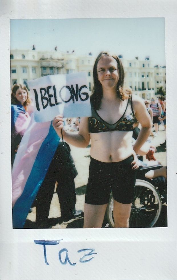 A person stands confidently holding a sign saying "I belong" at an outdoor event.