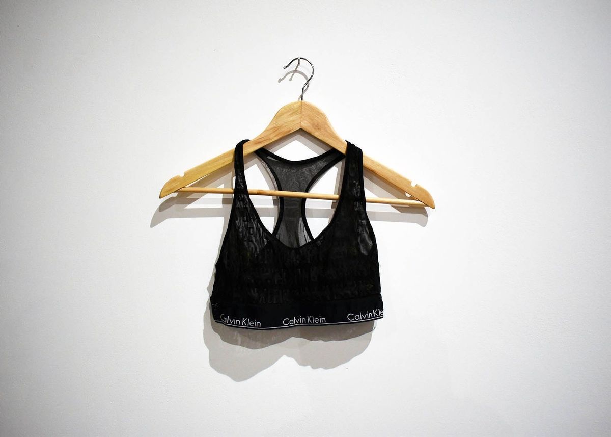 A black, sheer, Calvin Klein bra top on a wooden hanger.
