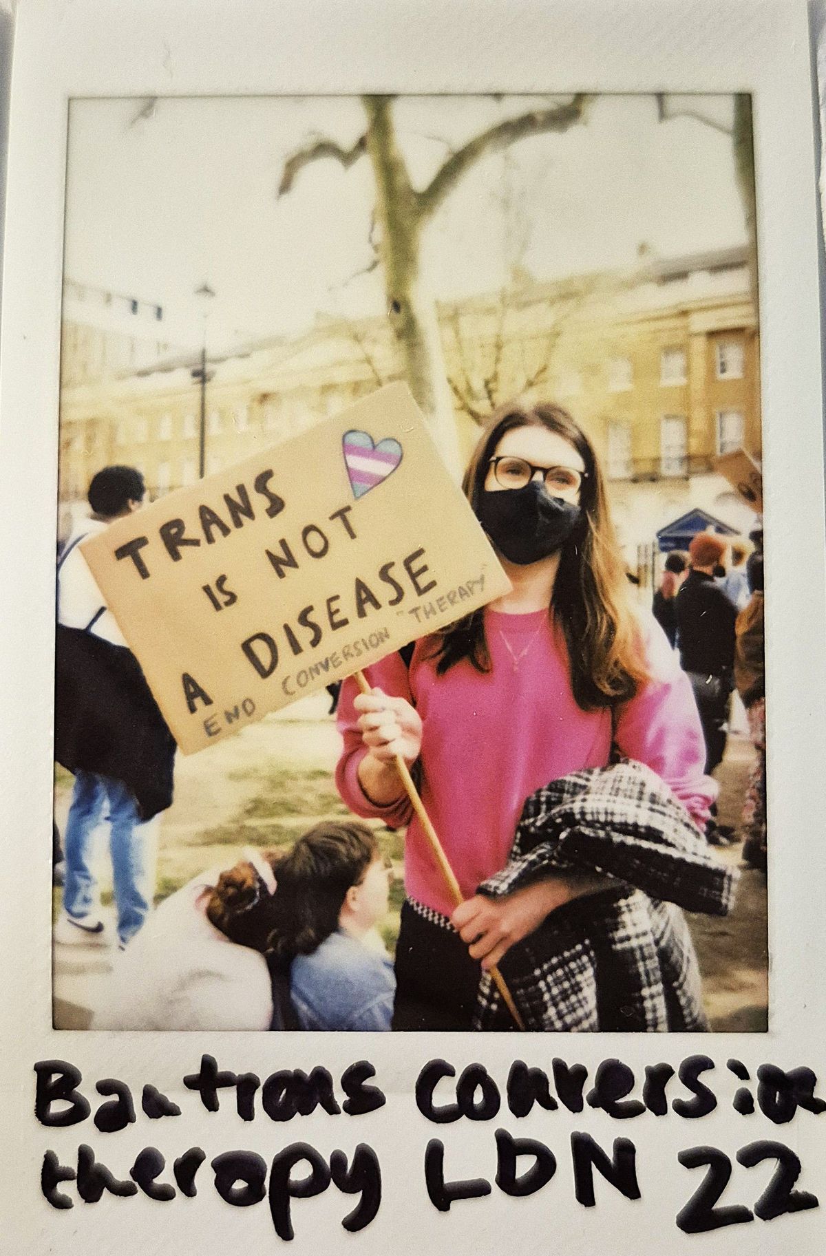 A person holding a sign which says "TRANS IS NOT A DISEASE END CONVERSION THERAPY".
