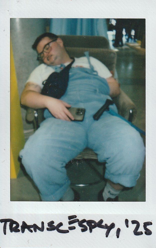 A person in overalls is asleep in a chair, holding a phone, looking quite comfortable and relaxed.