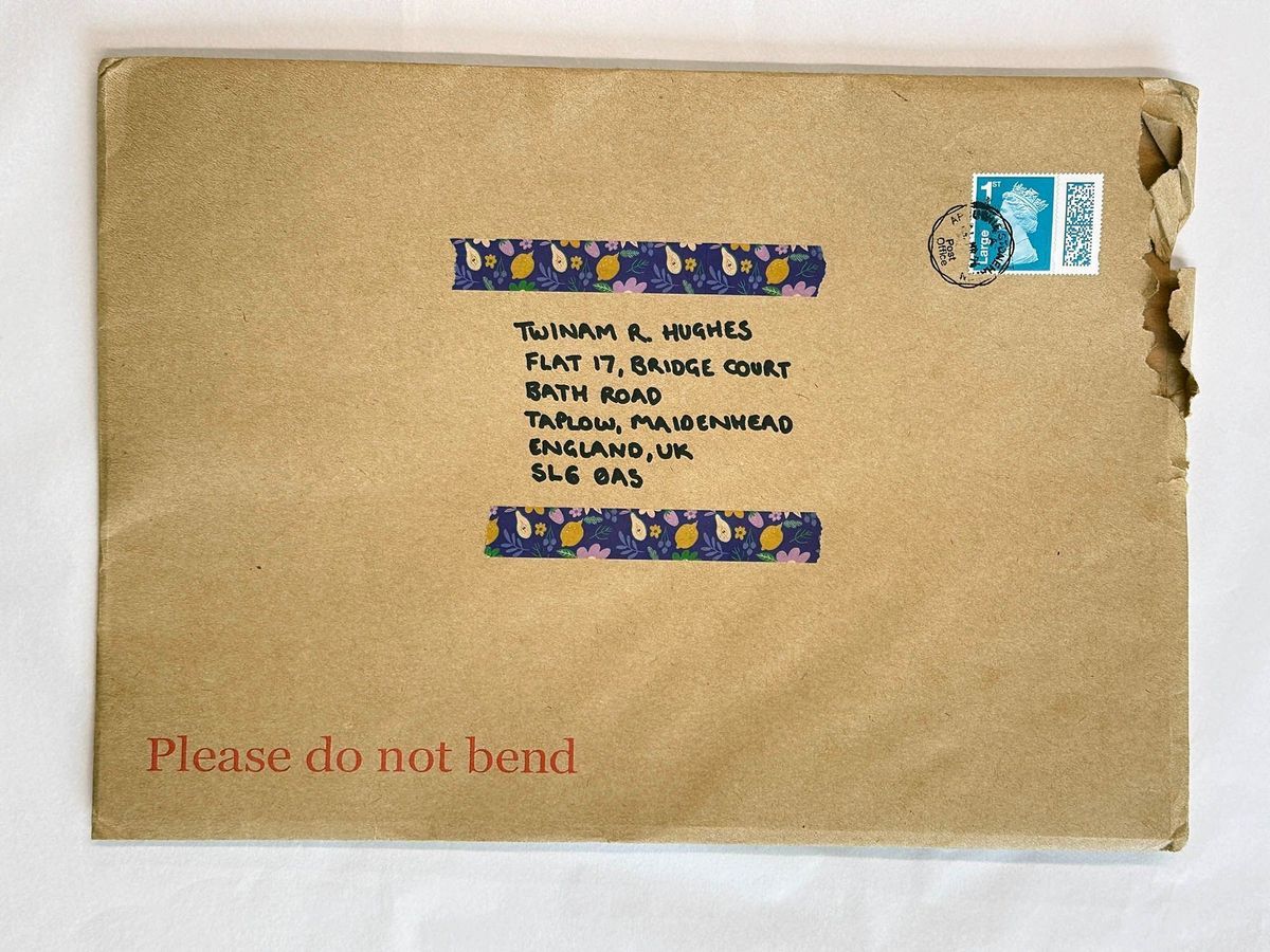 An opened brown envelope decorated with purple tape with flowers and fruit on. It has a franked 1st class stamp and the next "Please do not bend". It is addressed to the donor, Twinam R Hughes.