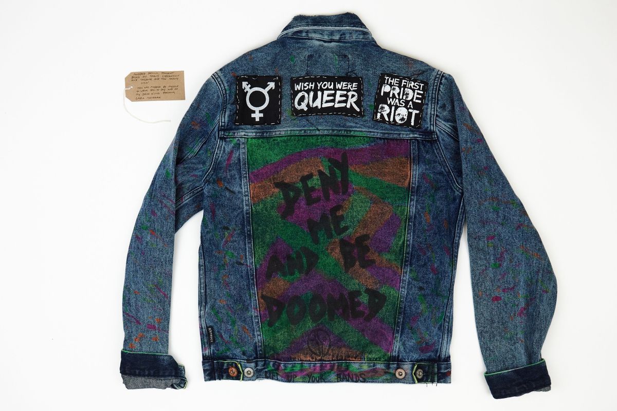 Modded denim jacket with queer/trans patches and slogan. With a brown handwritten luggage tag.