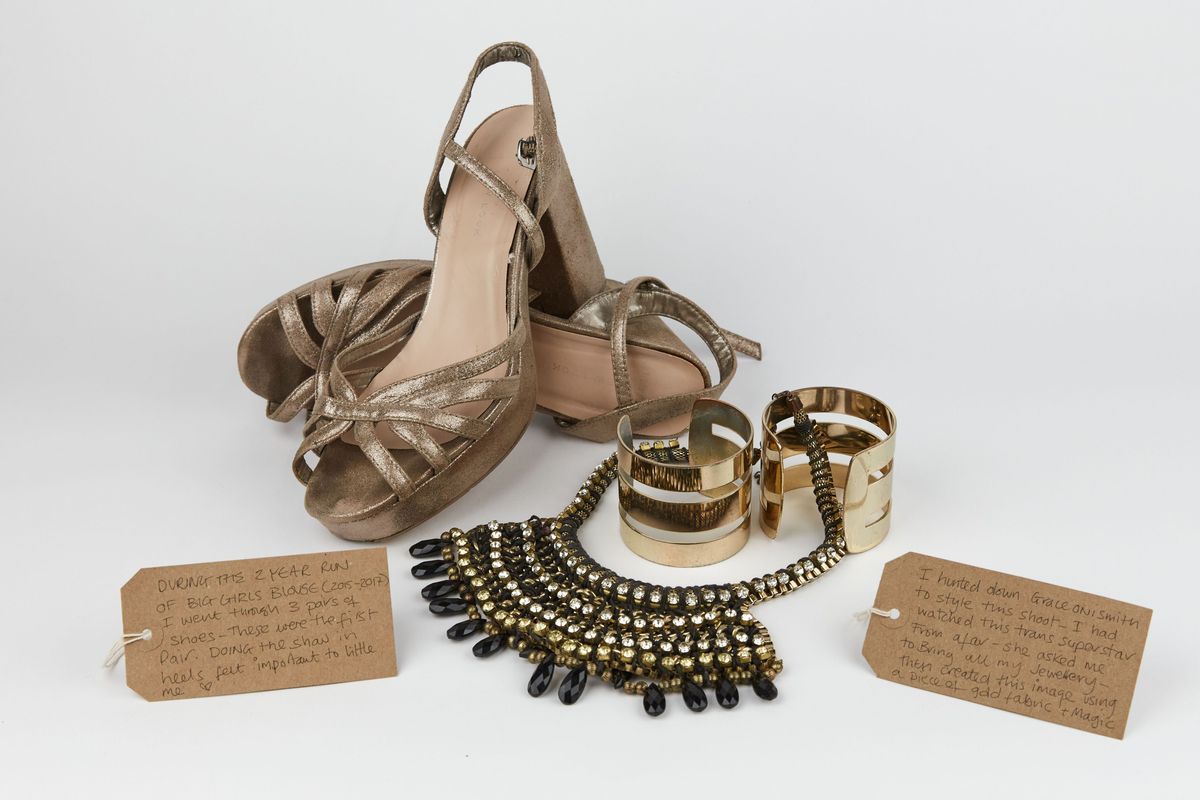 The image shows gold high heels, a statement necklace, and wide bracelets, accompanied by handwritten tags.