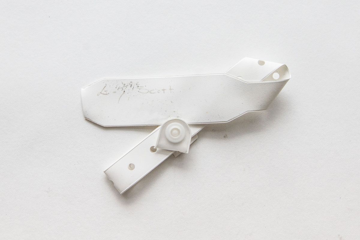 A white plastic garment tag with a circular, hole-punched fastener is placed against a plain background
