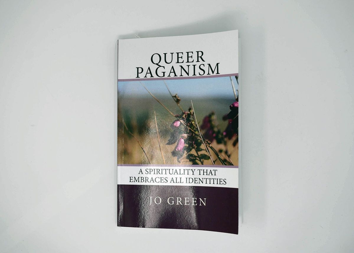 Front cover of a book titled "Queer Paganism - A spirituality that embraces all identities" by Jo Green. It also features a photo of a magenta flower and dry brush.