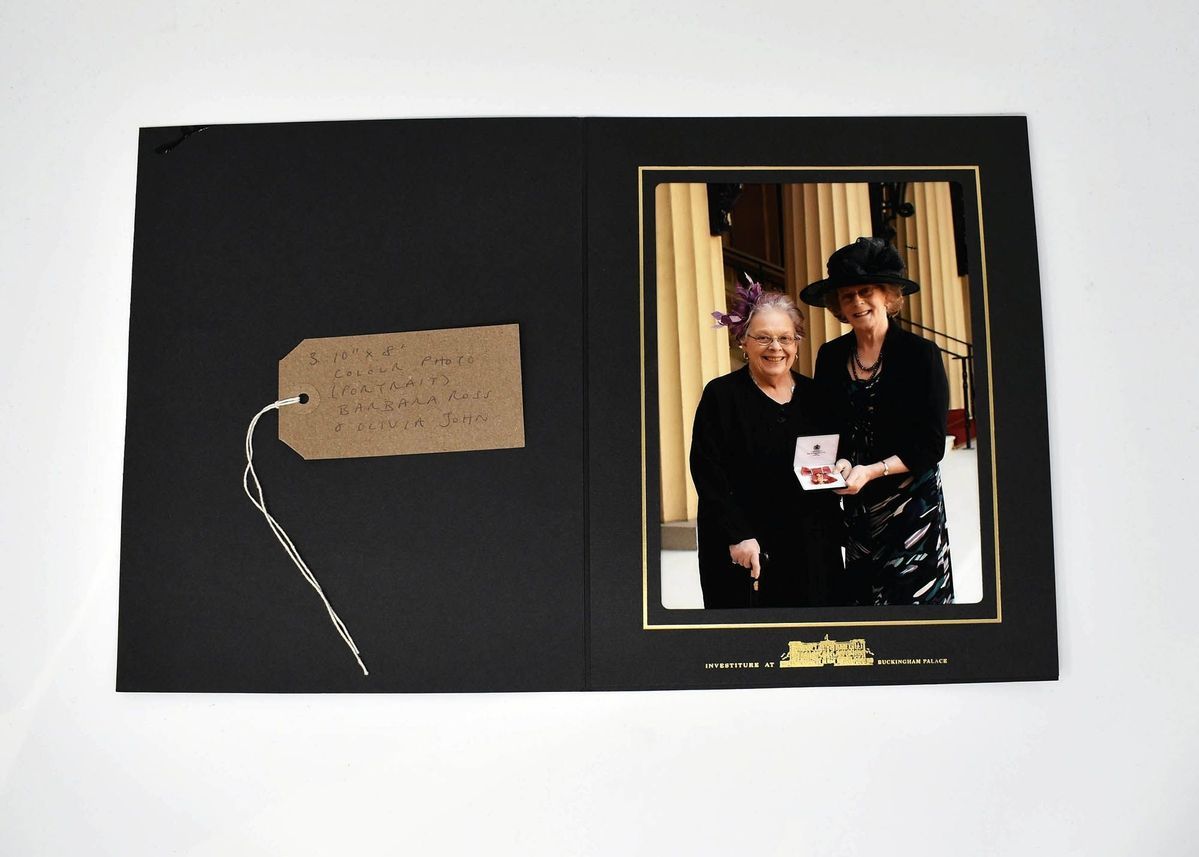 A black photo album holds an image of two women dressed formally, one holding a medal.