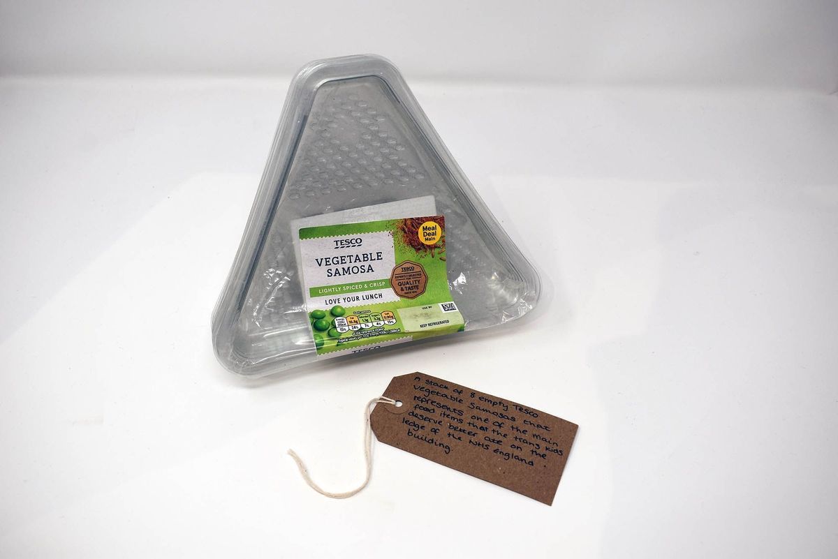 The image shows an empty triangle samosa package with a handwritten note beside it.