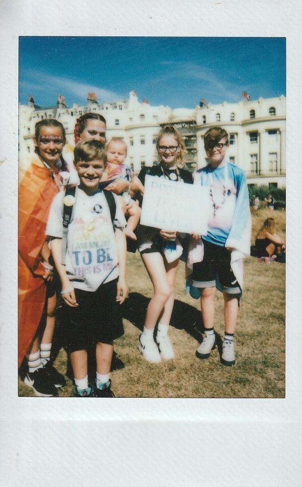 A group of people stand together, smiling outdoors, some holding protest signs.