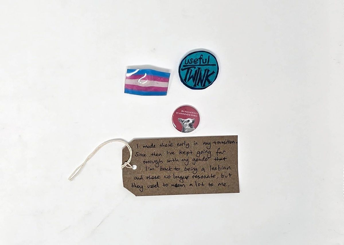 The image shows badges and a handwritten tag describing a personal transition journey.