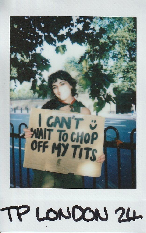 A person stands outdoors holding a sign expressing a personal message in front of trees.