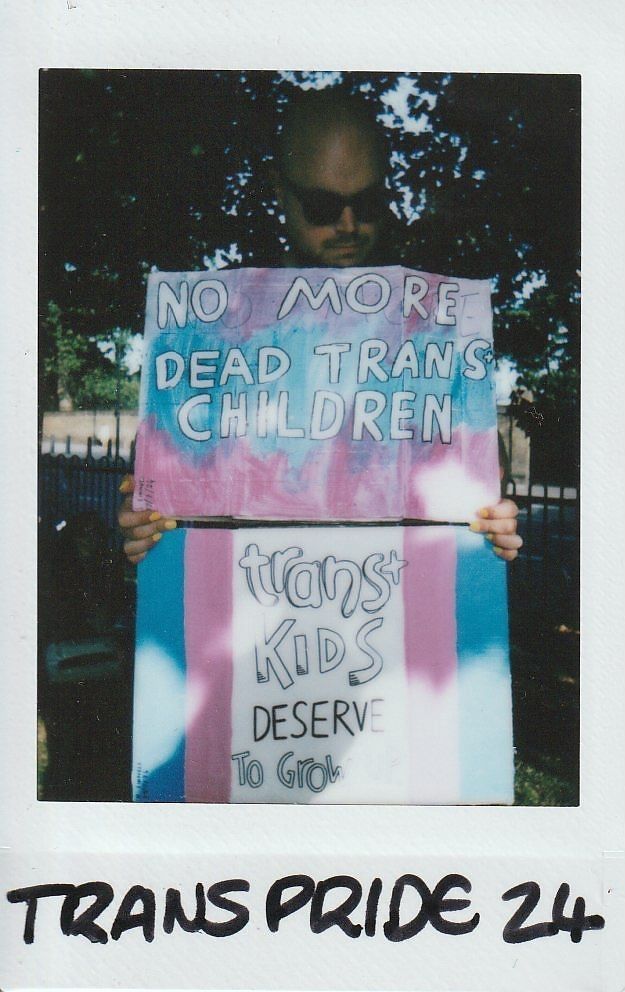 A person holds two signs with supportive messages for trans youth at Trans Pride event.