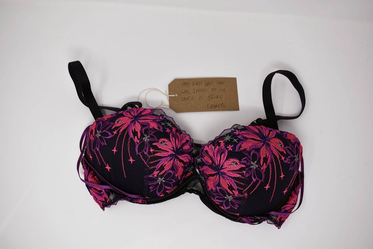 A black bra with pink and purple floral patterns is accompanied by a handwritten note luggage tag