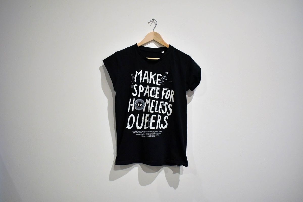 A black T-shirt with the text 'Make Space For Homeless Queers' hangs on a wooden hanger.