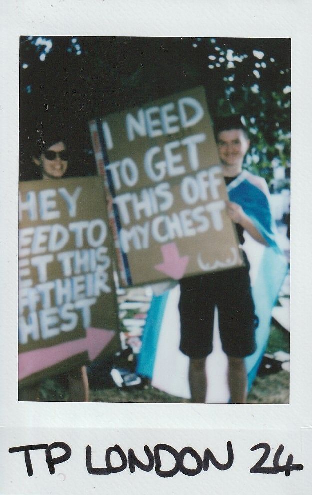 Two people are holding signs with bold messages while standing outdoors wearing different colored clothing.
