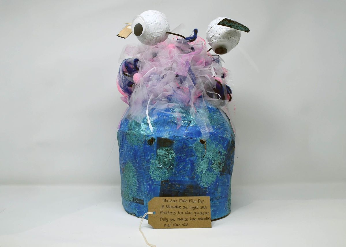 Handmade blue and green papier mache monster mask with colourful hair and googly eyes on stalks. Also a brown luggage tag.