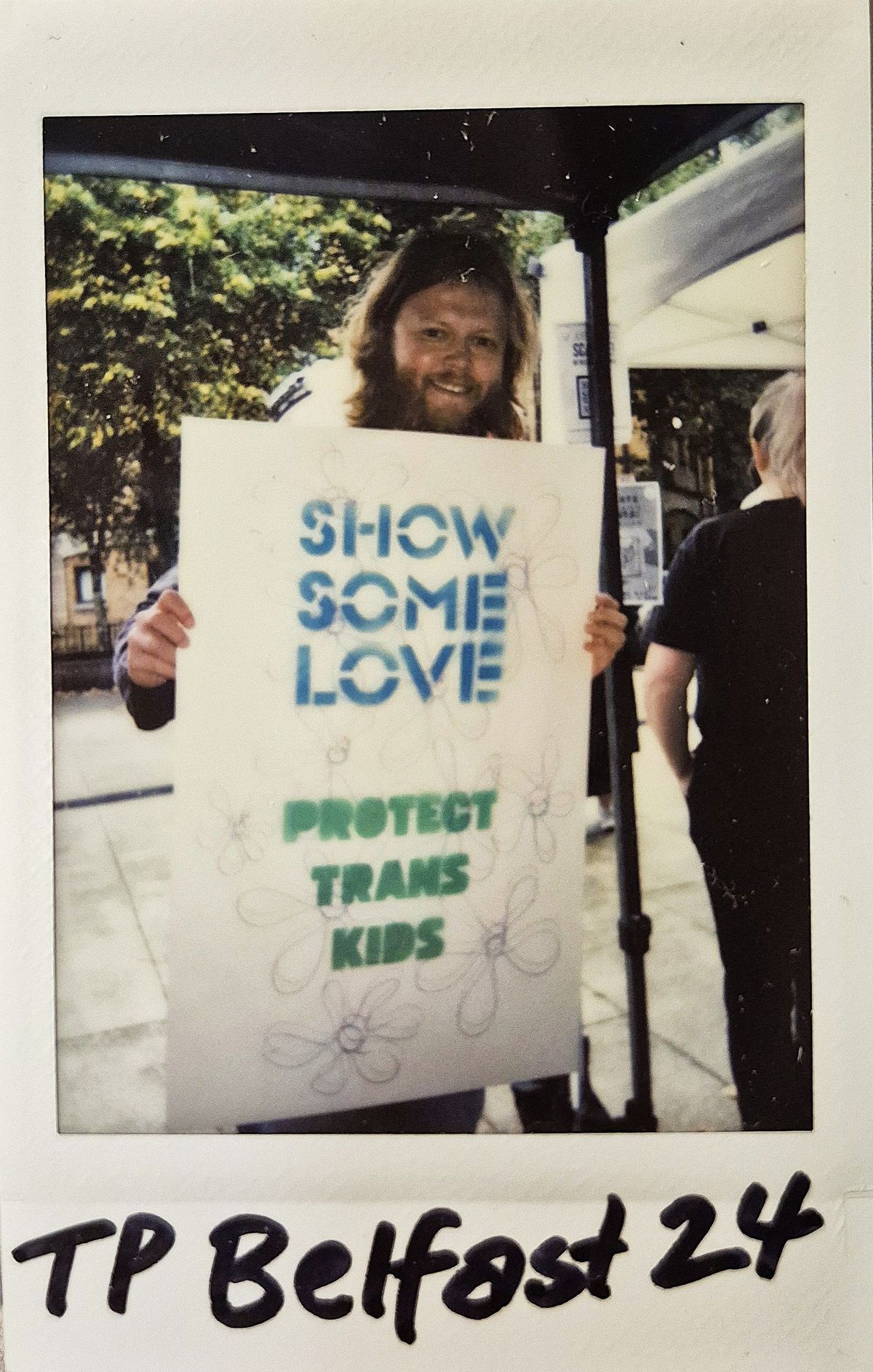 A person holds a sign reading "Show Some Love, Protect Trans Kids" during a pride.