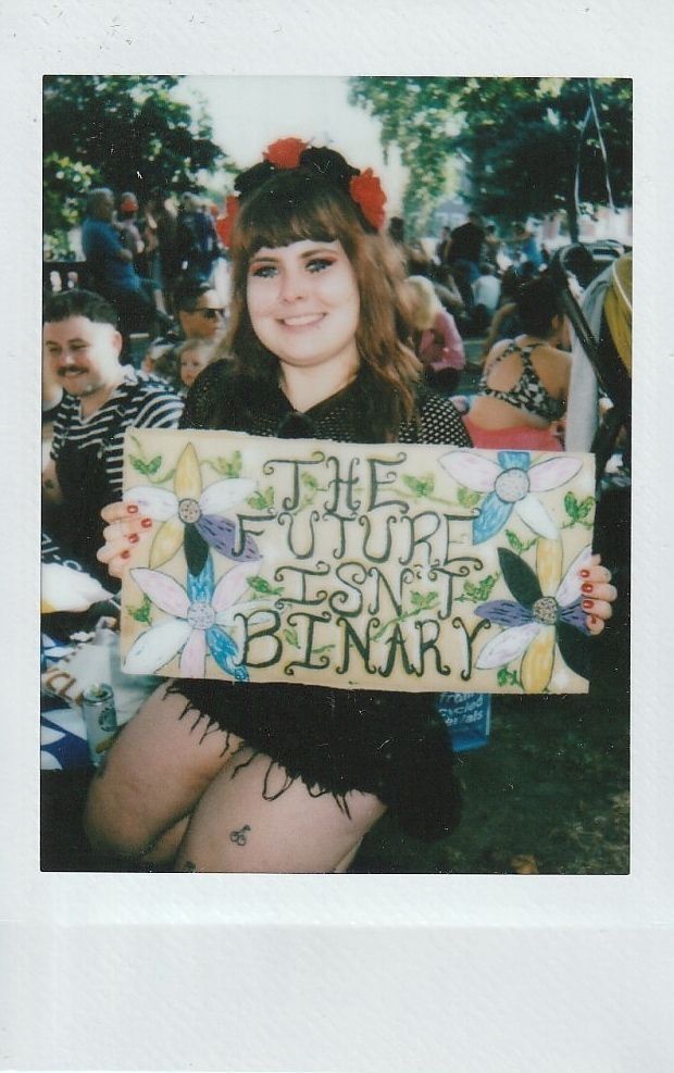 A person holds a sign saying "THE FUTURE ISN'T BINARY" surrounded by colorful flowers.