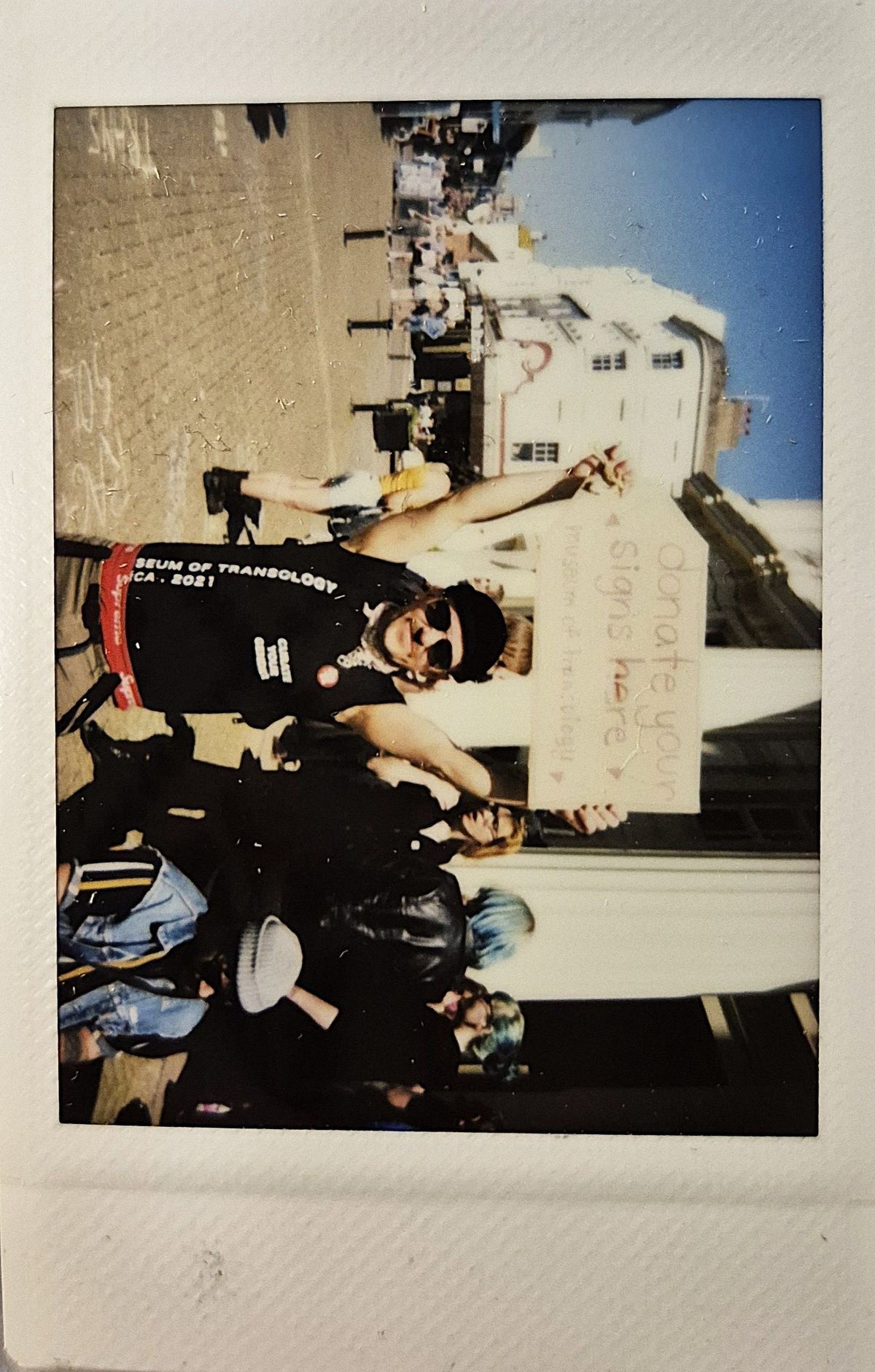 A person happily holds a sign reading “donate your signs here” while standing on a street.