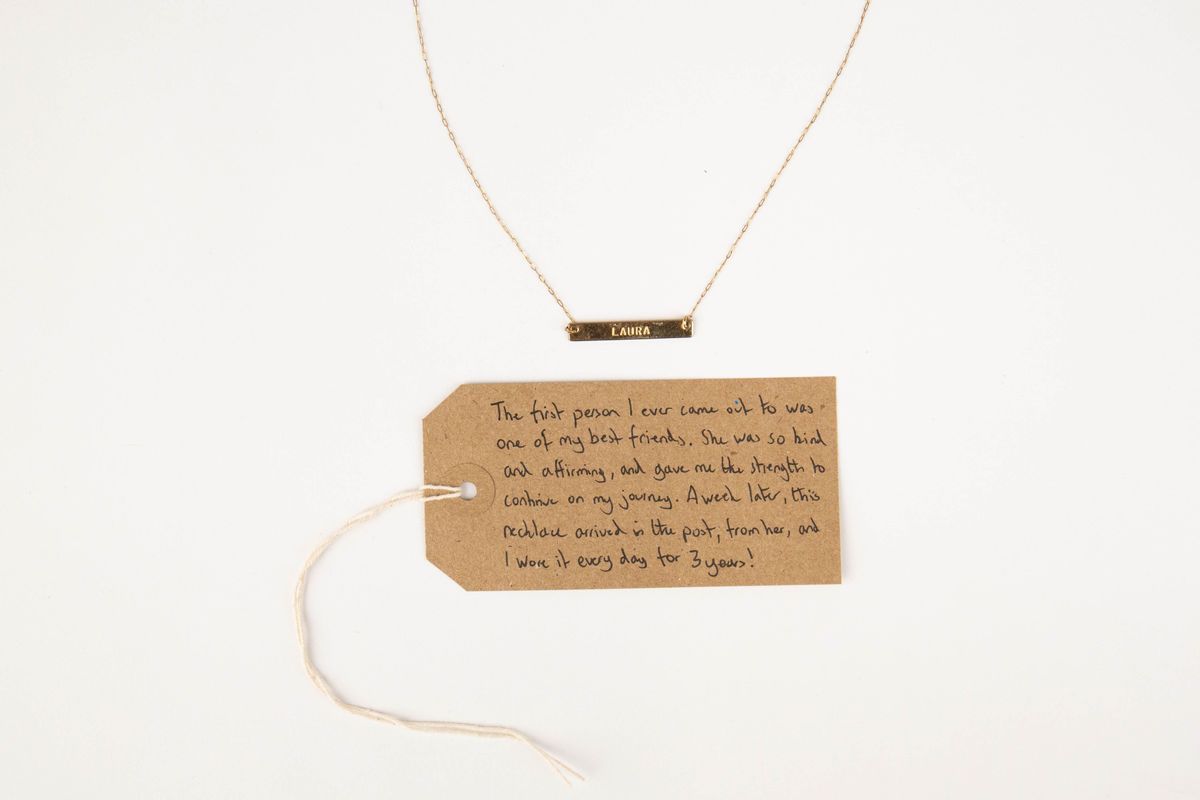 A gold necklace with name "LAURA". With a brown, handwritten luggage tag.