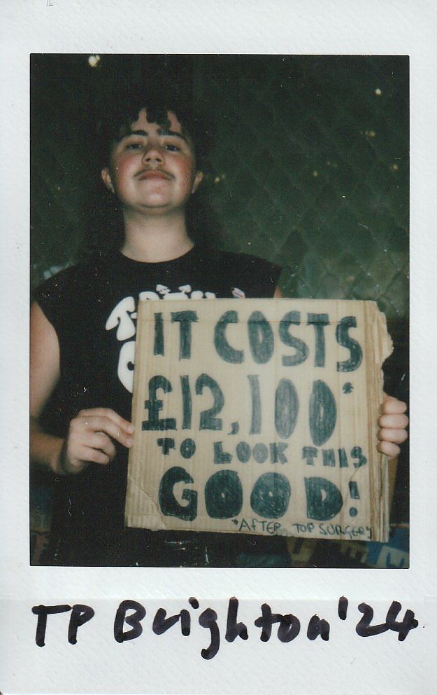 A person holds a cardboard sign that says "It costs £12,100 to look this good".