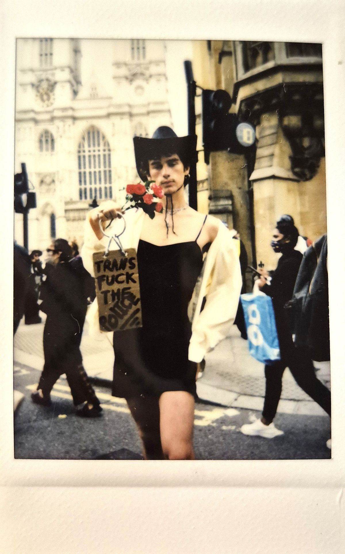 A person wearing a cowboy hat holds a sign and flowers during a street protest.