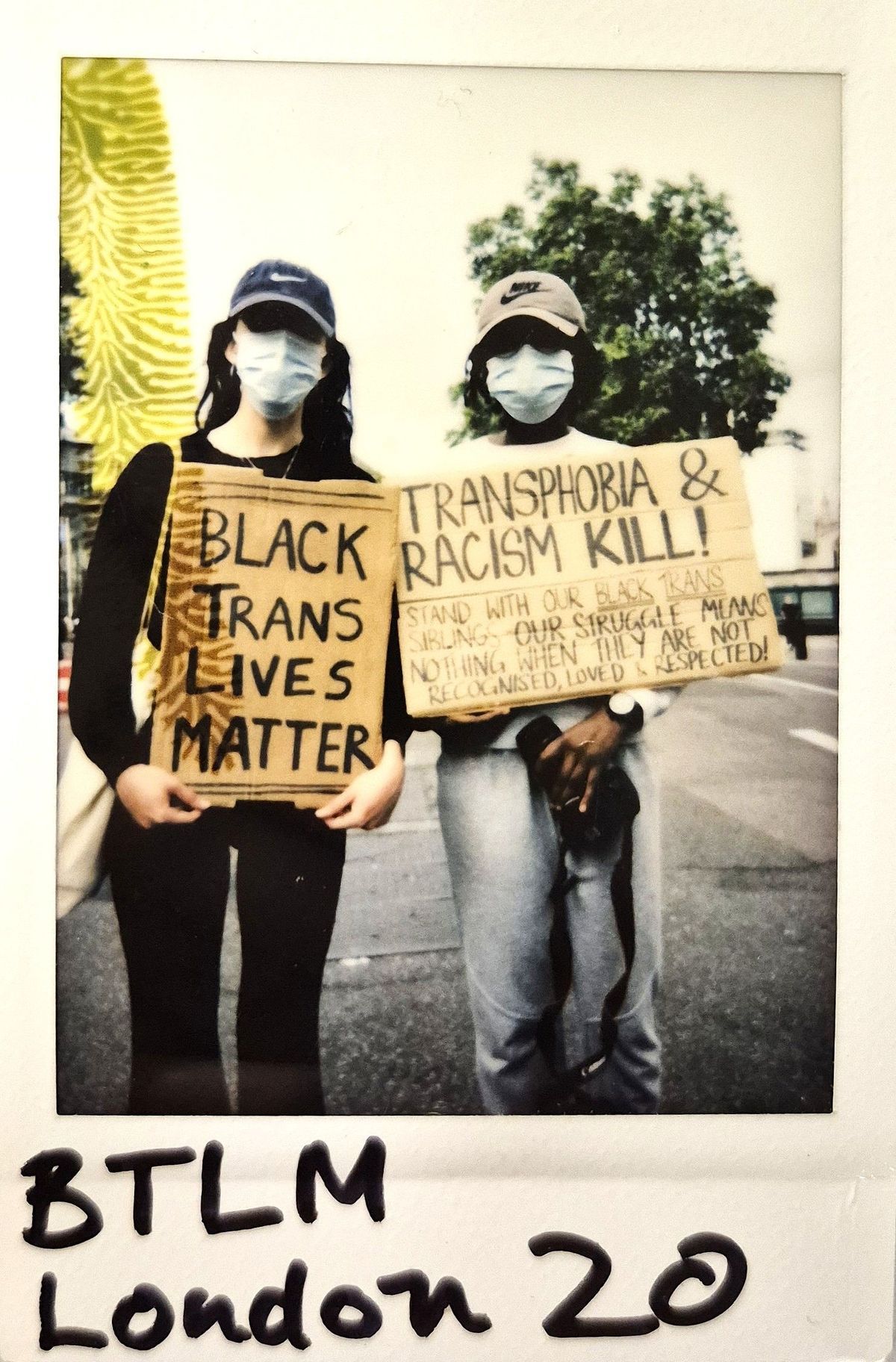 Two individuals at a protest hold signs advocating for Black trans lives and against transphobia and racism.