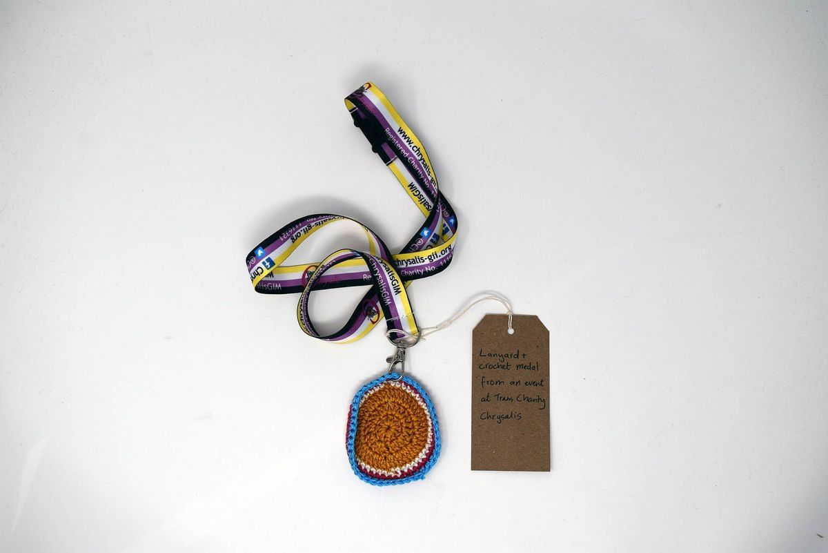 A colorful lanyard with a crocheted medal and a brown tag on a white background.