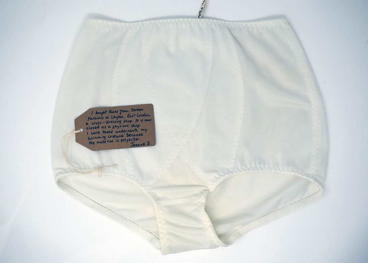 White underwear lying on a white surface. There is a brown tag with writing lay on the underwear.