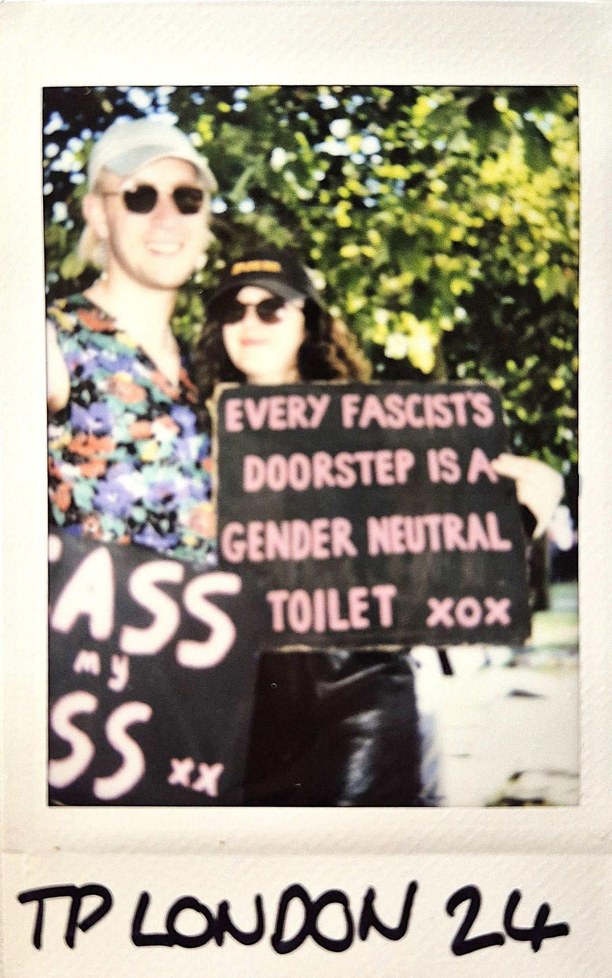 Two people are holding signs with a message about fascists, in a sunlit outdoor setting.